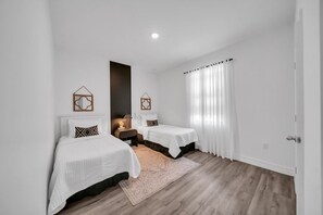 A bedroom with two beds, a nightstand, a rug, and a window with curtains.