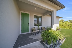A house entrance with a green door, a window, a small table with chairs, and a potted plant.