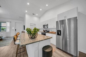 Cozinha moderna com ilha central, eletrodomésticos de aço inoxidável e vista para a sala de estar.