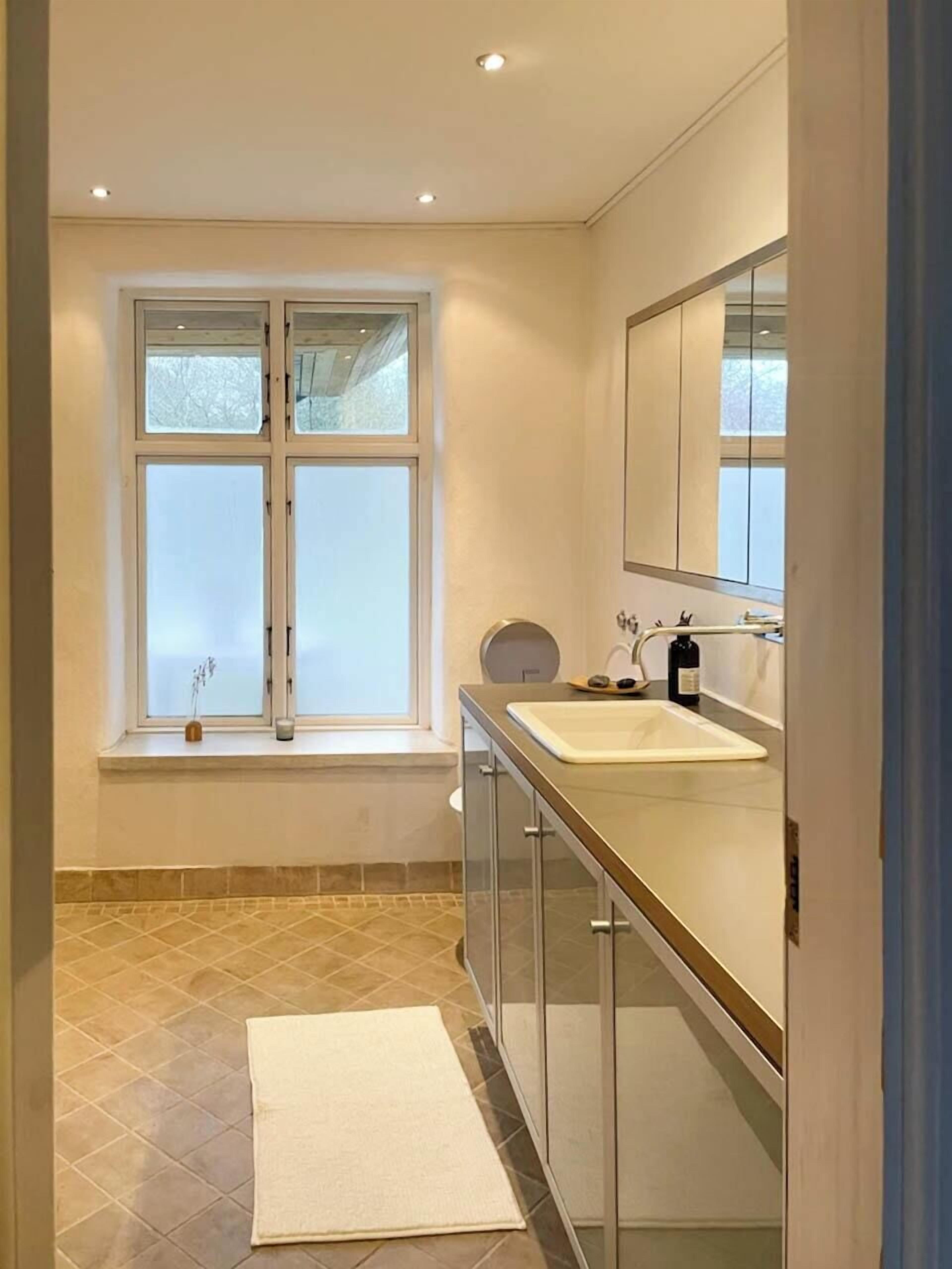 Un baño con ventana, lavamanos y espejo.