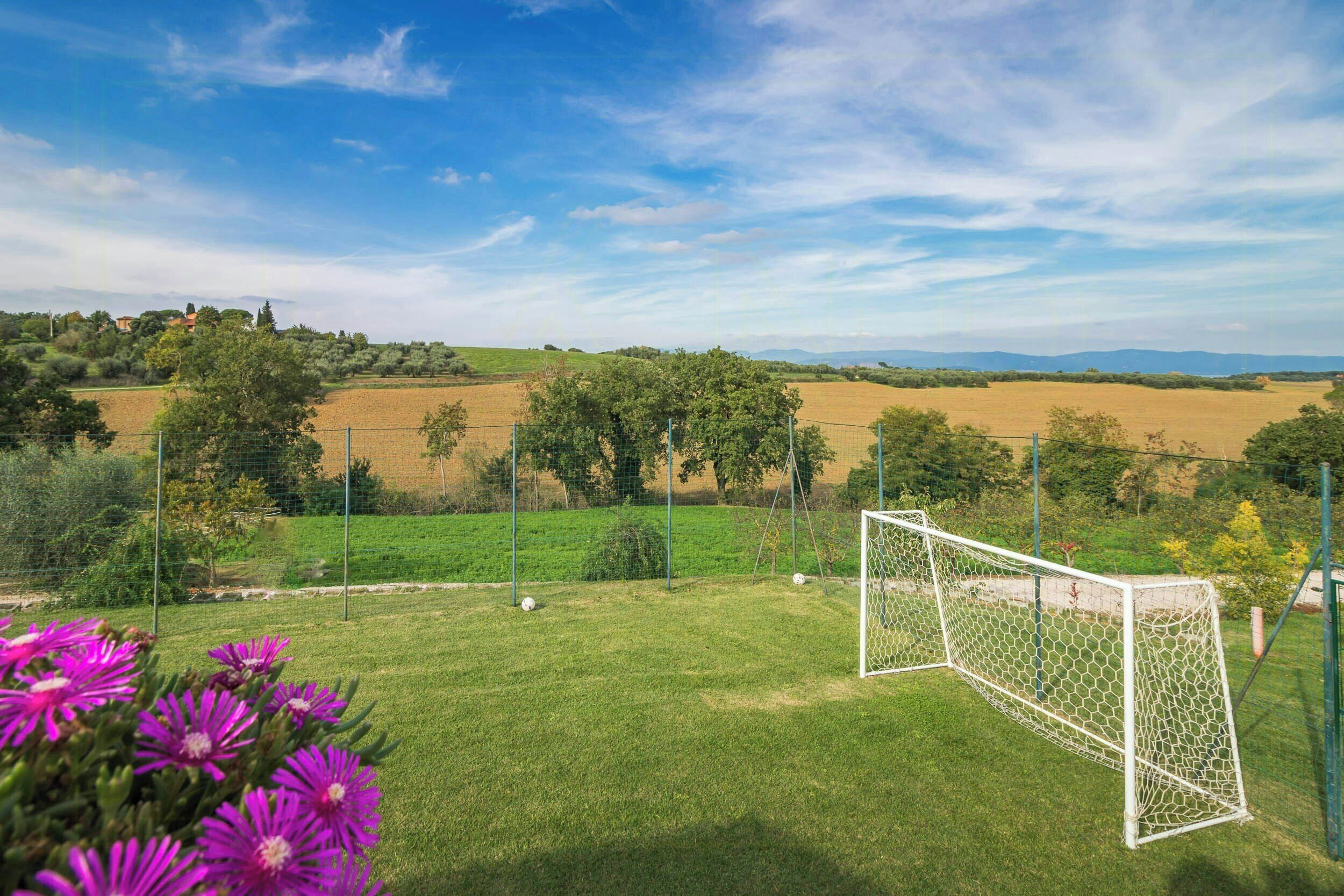 A soccer field with a goalpost, surrounded by green grass and trees, under a clear sky.