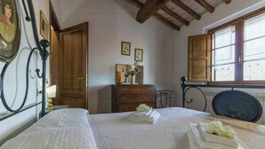 A neatly made bed with folded towels and a vase of flowers, wooden furniture, and a window with curtains. - Apartment with view of Lake Trasimeno (Castiglione del Lago)