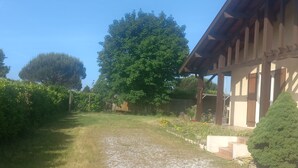 Un sendero de grava que conduce a un edificio con techo de madera y un jardín con árboles y arbustos.