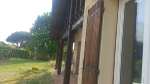Un edificio con un sendero de ladrillo que conduce a una puerta de madera, un espacio cubierto al aire libre y un patio césped con árboles.