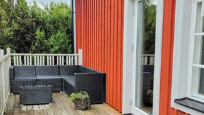 A wooden deck with outdoor furniture, a white fence, and a red building with a sliding glass door.