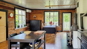 A rustic cabin interior with a dining area, kitchen, and large windows.