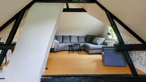 A loft bedroom with a sloped ceiling, a gray sectional sofa, a small round table, and a potted plant.