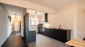A modern kitchen with a dark countertop, a black range hood, and a small dining area with a table and chairs. - Comfortable 2BR Apartment - Central Antwerp (Antwerp)