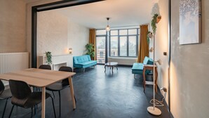 A modern living room with a large window, a sofa, a coffee table, and a dining area. - Comfortable 2BR Apartment - Central Antwerp (Antwerp)