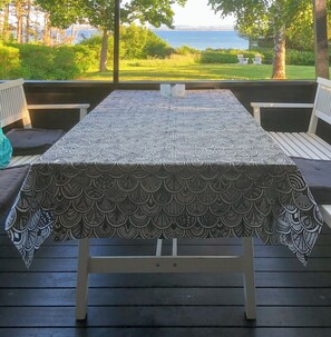 A covered outdoor dining area with a patterned tablecloth, wooden benches, and a view of the sea. - Peaceful home near Skødshoved beach (Dejret)