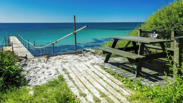A wooden pier leading to a sandy beach with a clear view of the ocean.