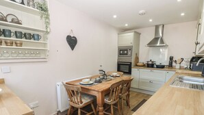 A kitchen with wooden cabinets, a built-in oven, a stainless steel range hood, and a dining table with chairs. - Banklands (Barnard Castle)