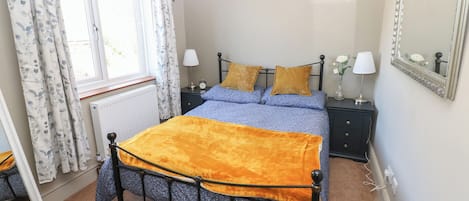 Un dormitorio con cama, mesita de noche, lámpara, espejo y ventana con cortinas.