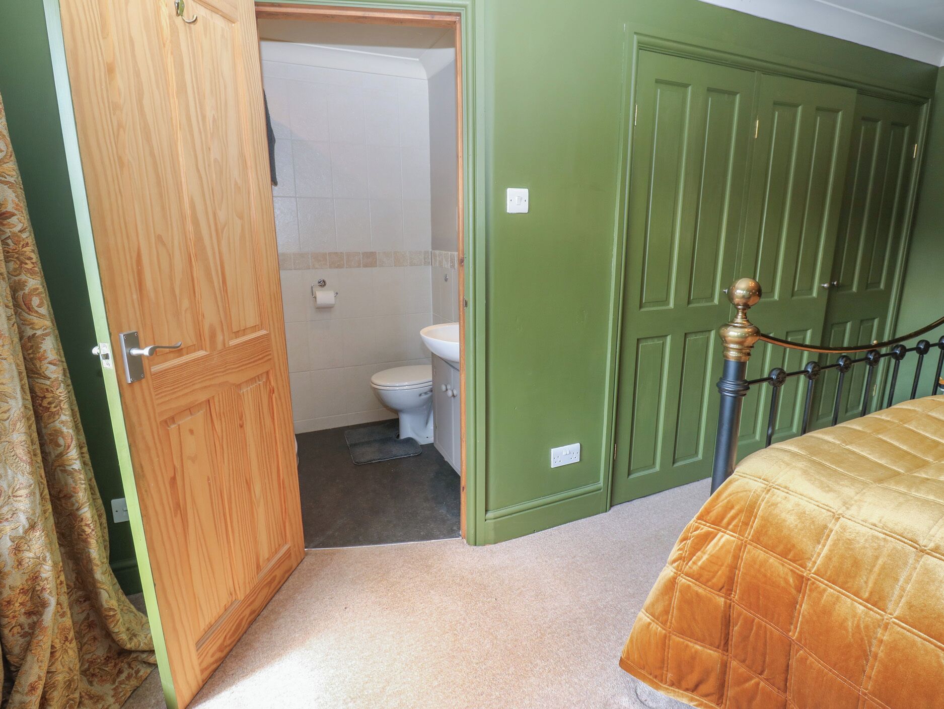 Un dormitorio con cama, puerta de madera, pared verde y baño con inodoro y ducha.