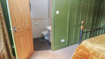 Un dormitorio con cama, puerta de madera, pared verde y baño con inodoro y ducha.
