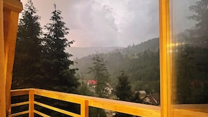 Une terrasse en bois, dotée d’une rambarde, qui offre une vue sur un paysage montagneux parsemé d’arbres et de maisons.
