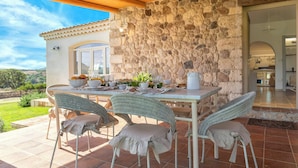 A covered patio with a stone wall, a dining table set with chairs, and a view of the countryside. - Luxury villa with heated pool in a vineyard (Mores)