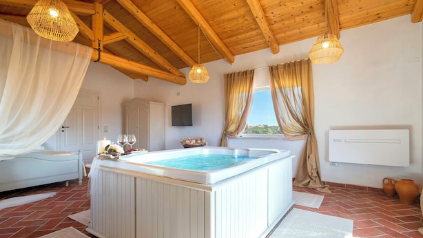 A room with a hot tub, wooden ceiling beams, a white radiator, and a view of the outdoors. - Luxury villa with heated pool in a vineyard (Mores)