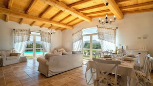 A spacious room with a wooden ceiling, a sofa, a dining table with chairs, and large windows with curtains. - Luxury villa with heated pool in a vineyard (Mores)