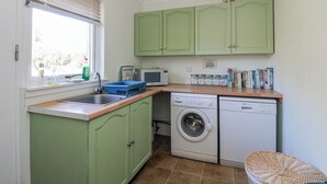 Una cocina compacta con armarios verdes, lavadora, microondas y ventana con persianas.