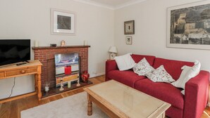 Una sala de estar con televisor, chimenea, sofá rojo y un cuadro en la pared.