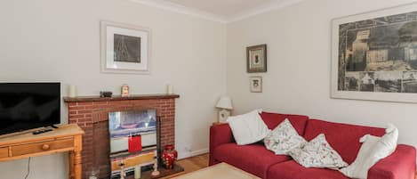 A living room with a TV, fireplace, red sofa, and a painting on the wall.