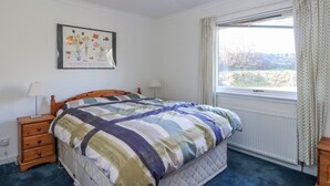 Un dormitorio con cama, mesitas de noche, ventana con cortinas, radiador e iluminación de pared.