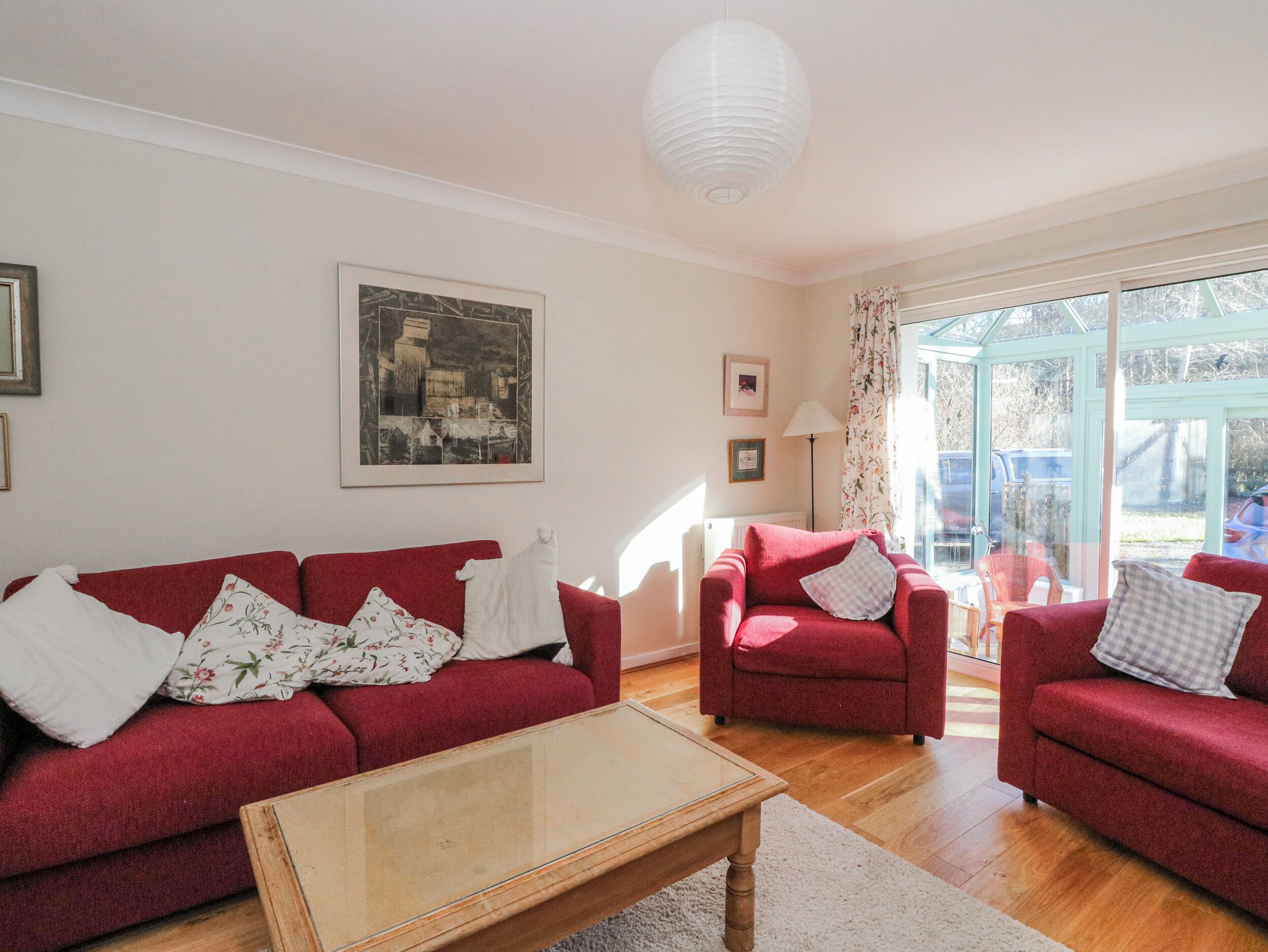 A living room with a red sofa, a glass coffee table, and a view of the outside through a glass door.