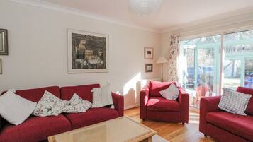 A living room with a red sofa, a glass coffee table, and a view of the outside through a glass door.