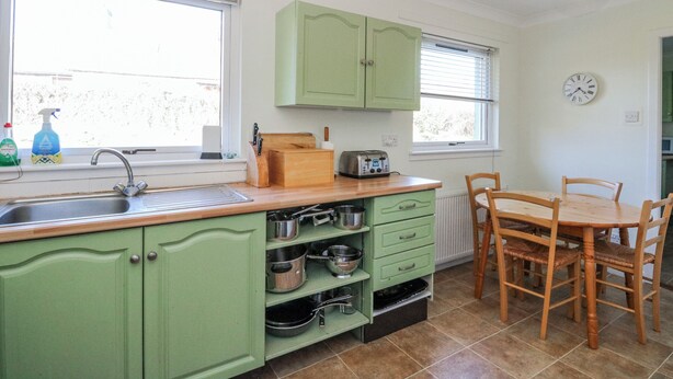 Una cocina con armarios verdes, un lavamanos, un tostador y una mesa de comedor con sillas.