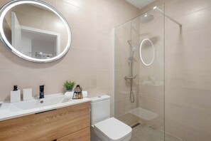 A modern bathroom with a glass-enclosed shower, a round mirror, a white sink, and a toilet. - Modern 2BR Marbella Centre Pool & Terrace (Marbella)