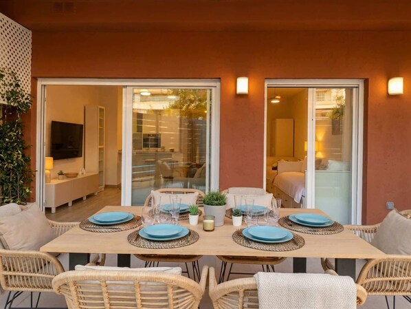 A dining area with a table set for four, surrounded by wicker chairs, and a glass partition separating it from the adjacent living space. - Modern 2BR Marbella Centre Pool & Terrace (Marbella)