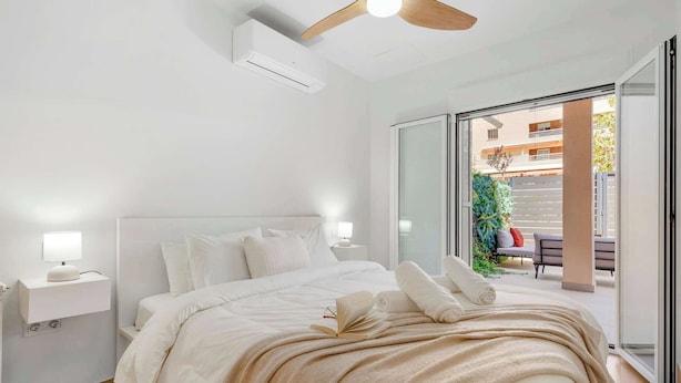 Une chambre à coucher comprenant un lit, des lampes de chevet, un ventilateur de plafond et une porte-fenêtre coulissante donnant sur un espace extérieur.