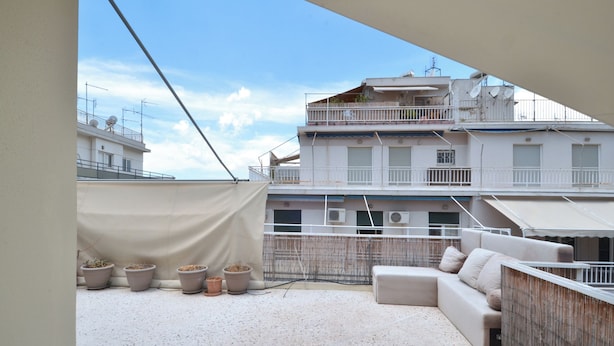 Terraza en la azotea con un sofá, plantas en macetas y vistas a edificios.