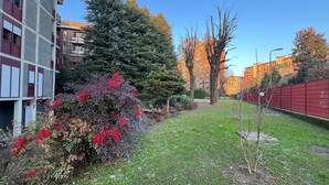 A residential area with a grassy lawn, a red fence, and a multi-story building with balconies. - San Siro Suite – Elegant Room Near San Siro (With Host) (Milan)