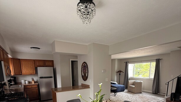 A modern kitchen with wooden cabinets, a stainless steel refrigerator, and a dining area with a round table and chairs. - This beautiful 3-bedroom condo in Painesville has the comforts of home, elevated (Painesville)