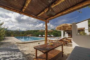 A wooden pergola over a pool area with lounge chairs and a table with glasses. - 5-bedroom Villa Near Southwest Beaches (Sant Antoni de Portmany)
