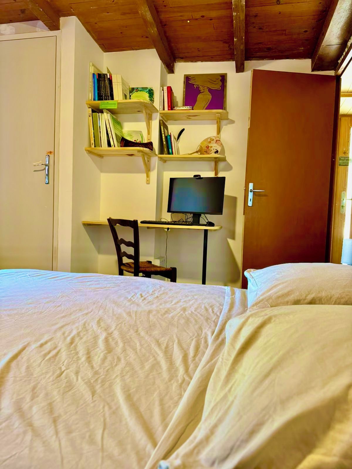 Un dormitorio con cama, un escritorio con computadora y estanterías con libros y objetos decorativos.