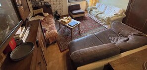 Ein kompakter Wohnbereich mit Sofa, einem kleinen Couchtisch, einem gemusterten Teppich und einem Esstisch mit Stühlen.
