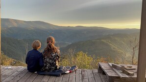 Två personer sitter på ett trädäck med utsikt över ett bergigt landskap.
