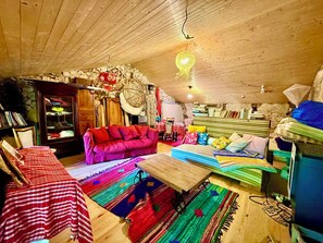 Une pièce mansardée chaleureuse avec un plafond en bois, un canapé rouge, un lit avec une literie colorée et divers objets de décoration.