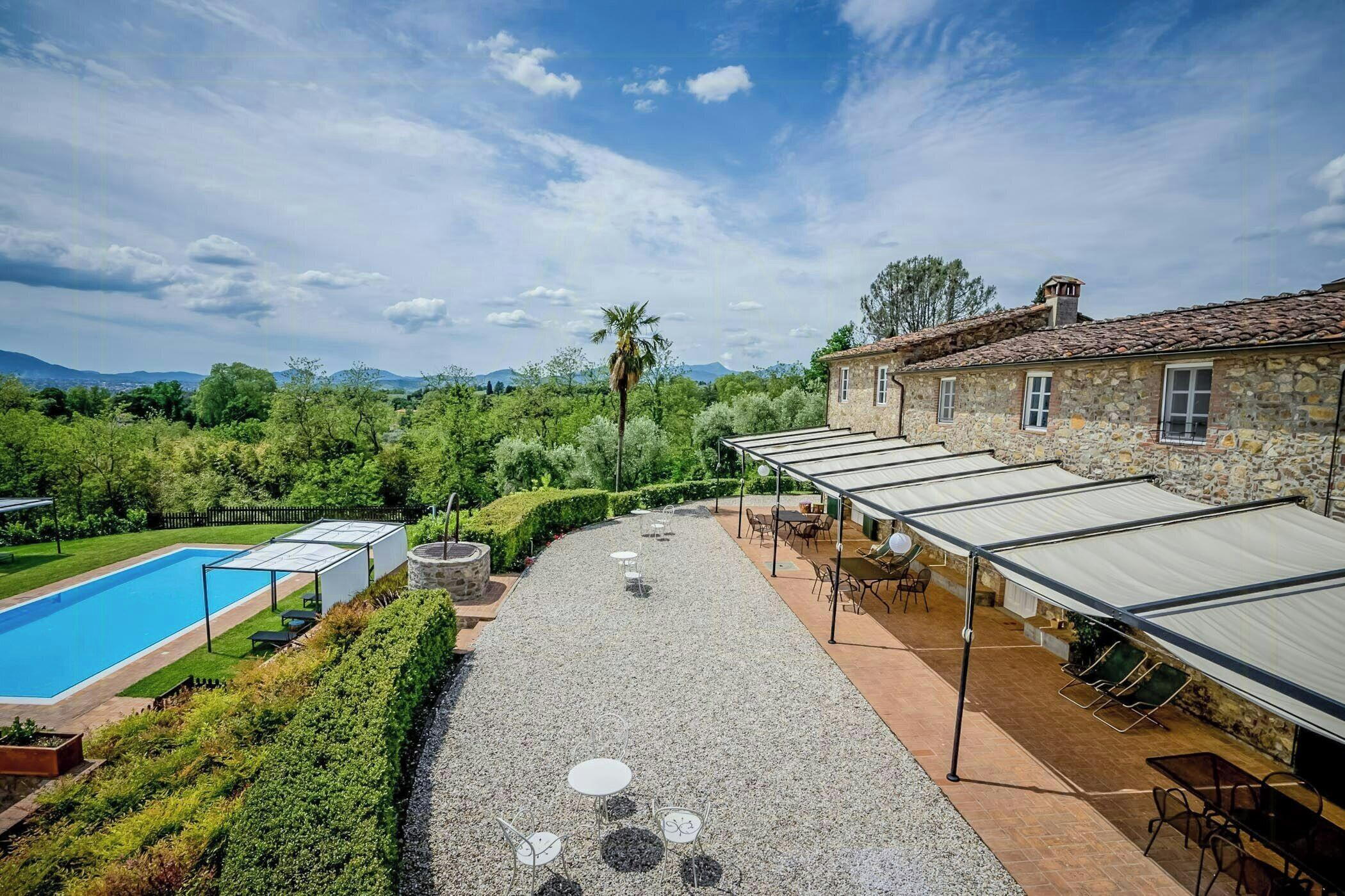 Una piscina, area salotto all'aperto e un edificio in pietra con tetto in tegole.