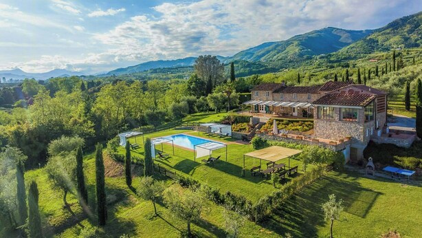 Une grande maison avec une piscine, entourée d’une végétation luxuriante et de montagnes.