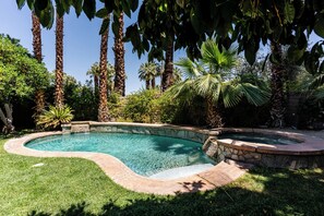 A landscaped pool area with a curved design, surrounded by palm trees and various shrubs. - Rancho Estates Retreat (Rancho Mirage)