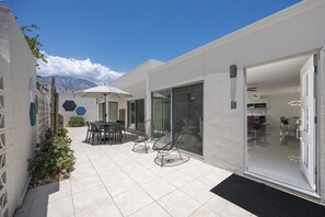 Eine moderne Terrassenanlage im Freien mit Tisch, Stühlen, einem Glastür-Eingang und Blick auf die Berge.