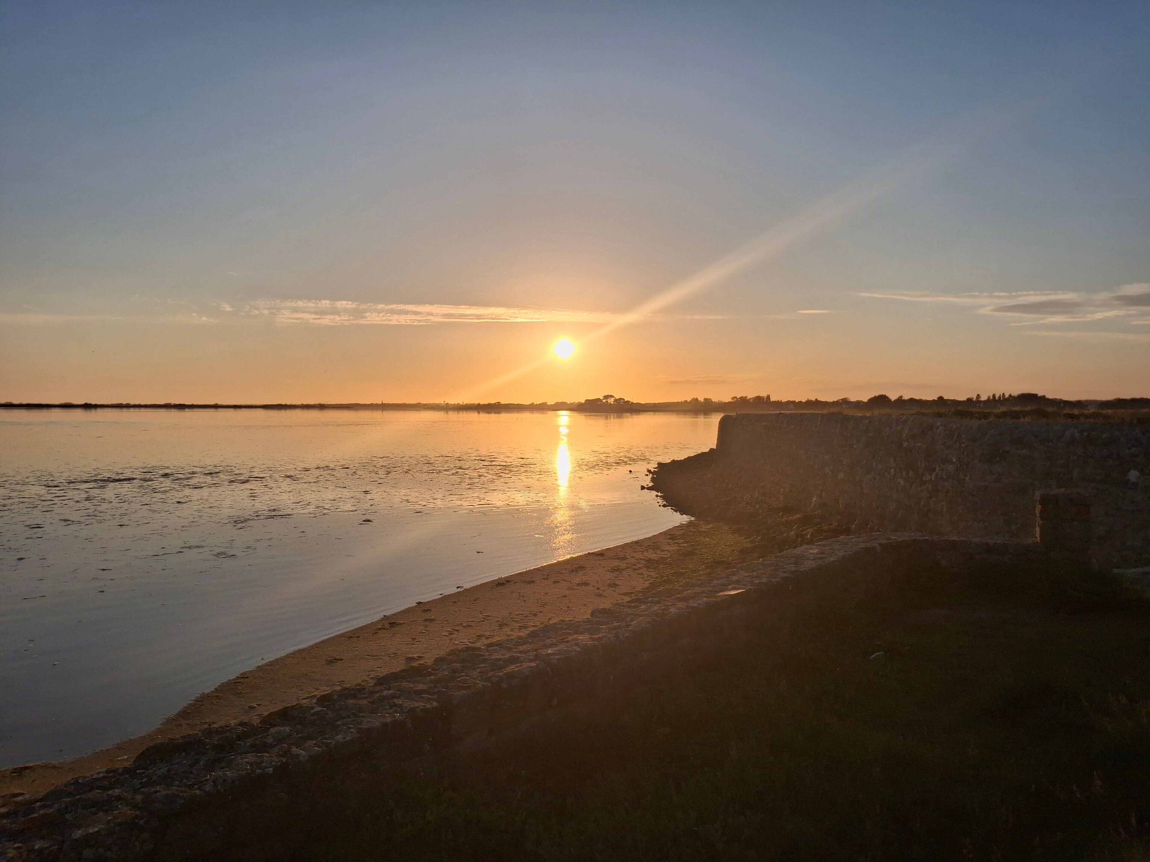 A sunset over a calm body of water with a stone wall on the right.