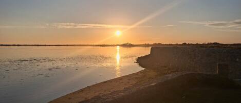 A sunset over a calm body of water with a stone wall on the right.