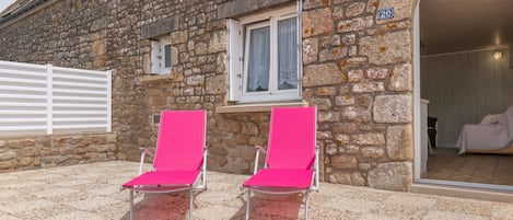 Un edificio de piedra con un cartel con el número 20, una ventana con cortinas de encaje y dos sillones lounge rosados afuera.