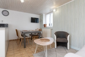 Un coin repas comprenant une table, des chaises, un téléviseur et une fenêtre avec des rideaux.