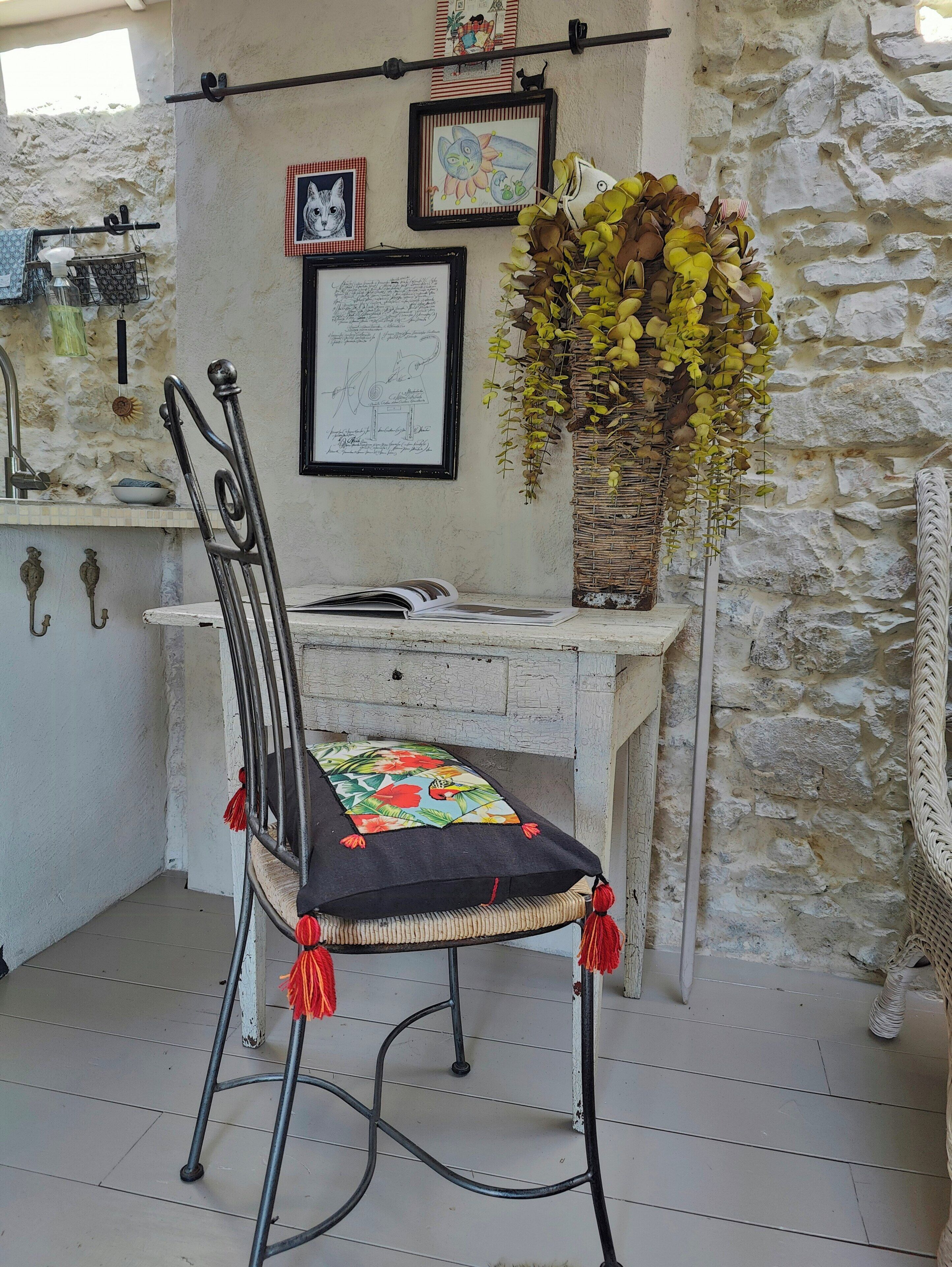 A rustic stone wall, a metal chair with a cushion, a desk with a map, and a hanging basket of yellow flowers.